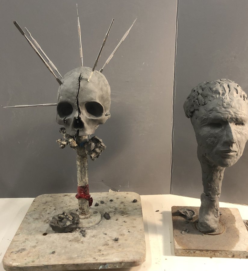 Skull and Head — two clay sculptures on the studio bench, one a spiked skull