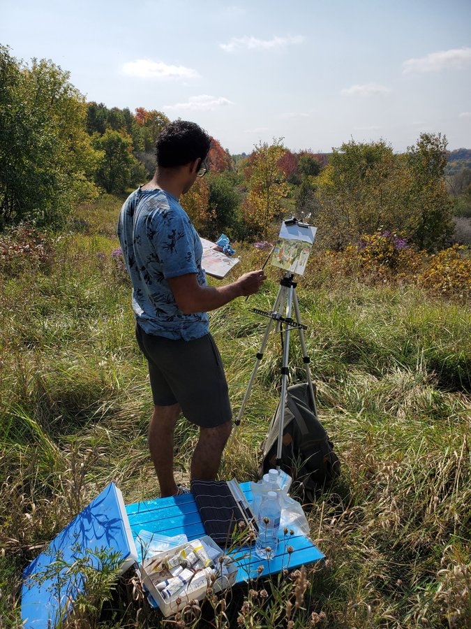 Usman painting en plein air at an easel in a meadow